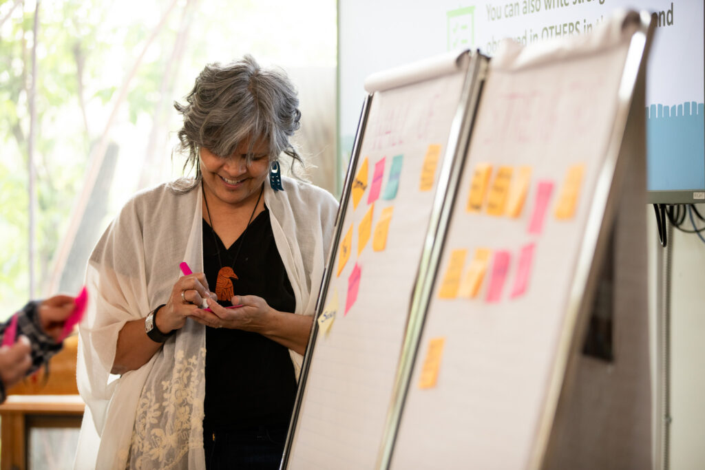 a person writes on a sticky note in front of a presentation board