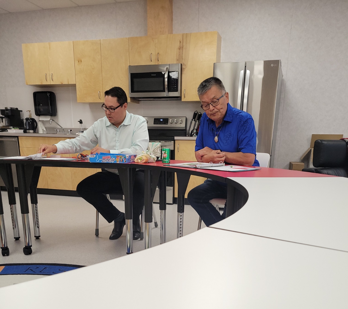 2 people sit with open binders at a circular table