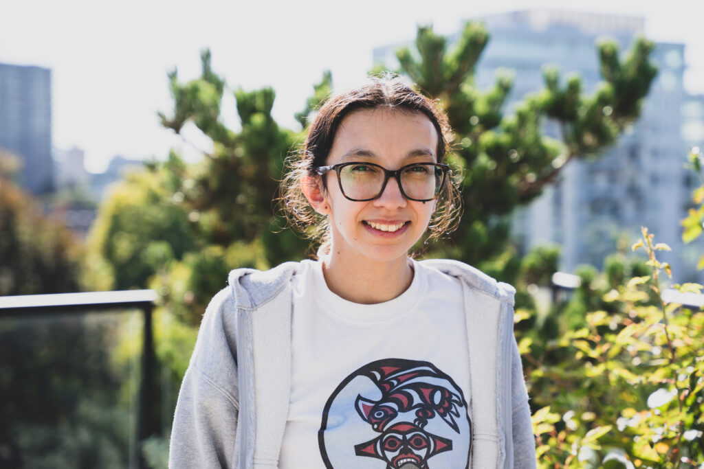 Sarah stands and smiles outside on a balcony on sunny day