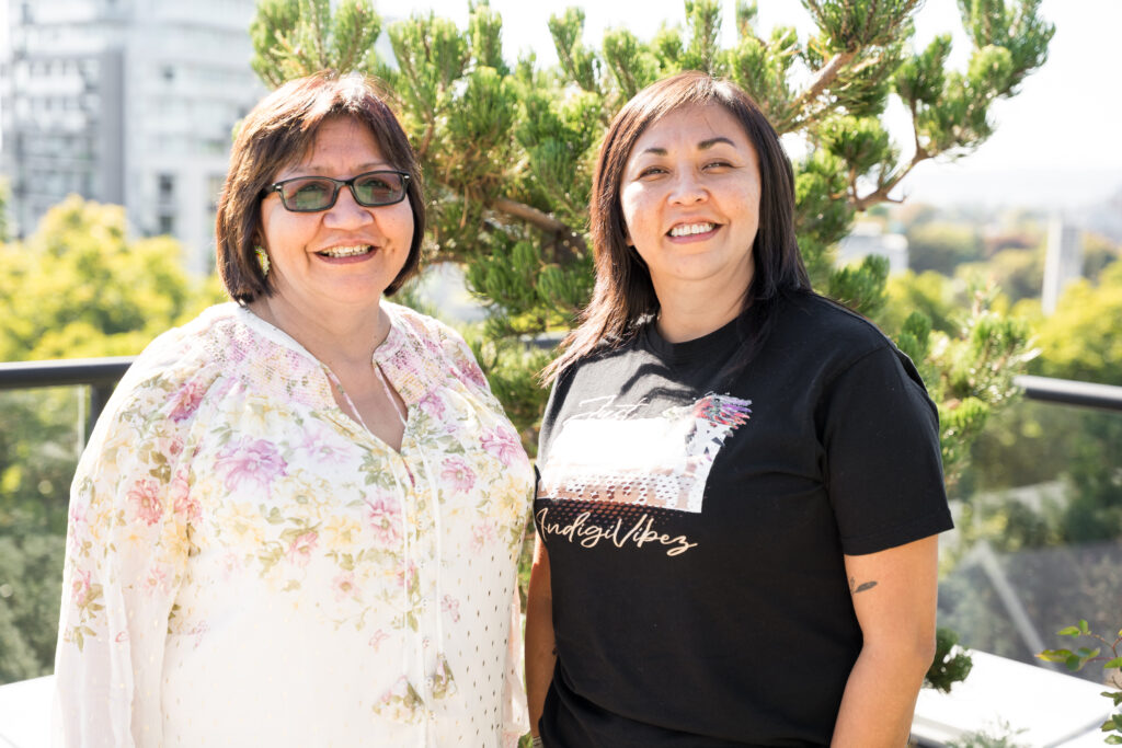 Sisters stand side by side smiling on a sunny patio