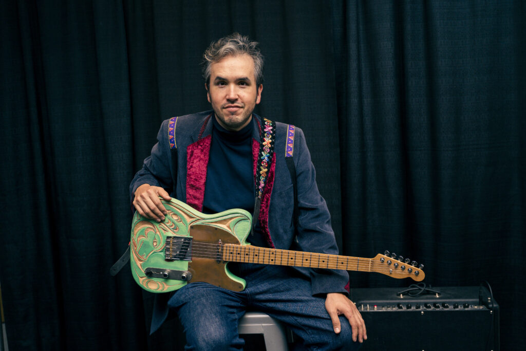 Musician poses for a photo with his guitar carved in Coast Salish art style