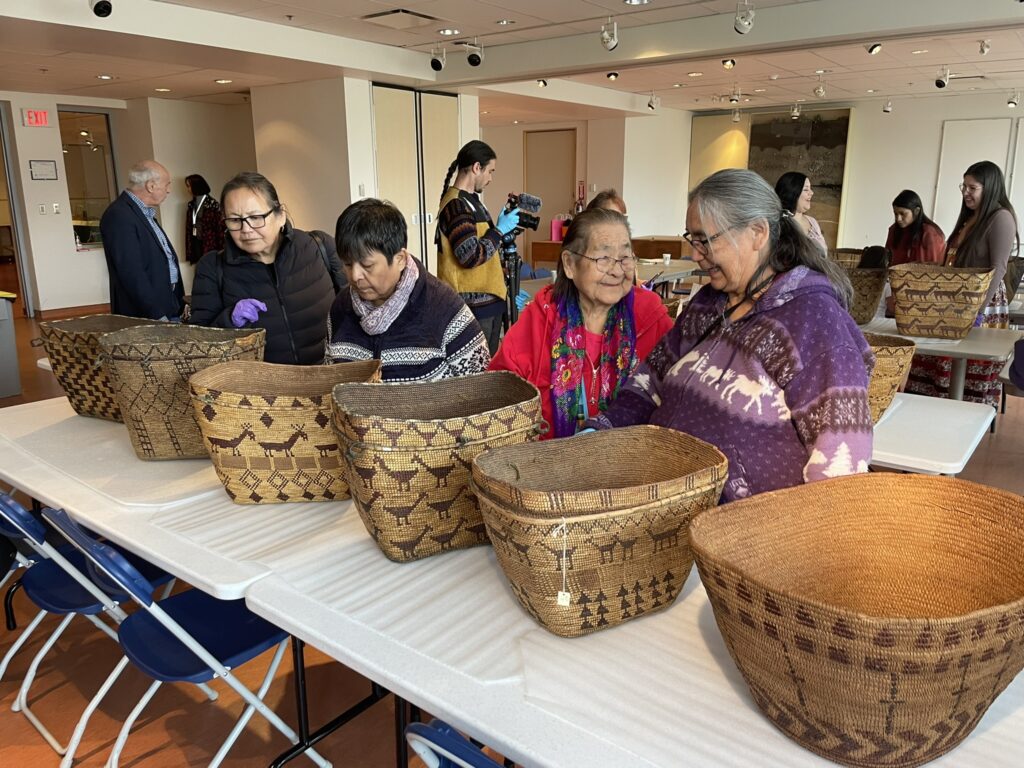 People look at woven baskets displayed on long tables. The baskets feature intricate animal designs and various other shapes.